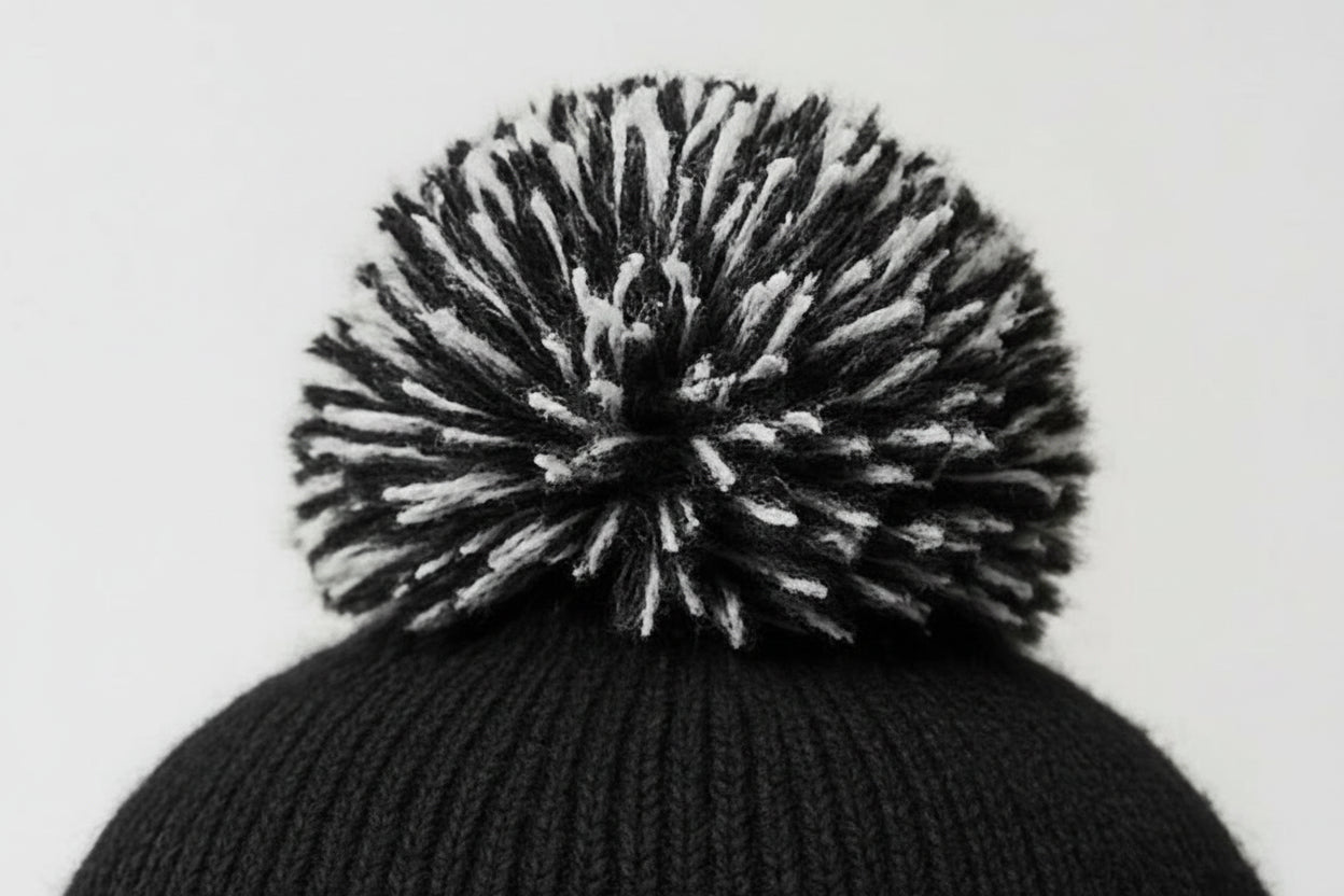 Black knit beanie with a large pom-pom on a light gray background