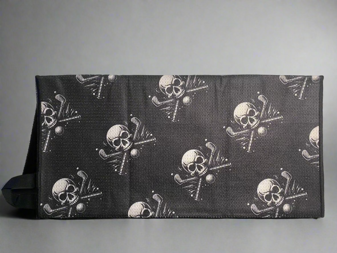 Black towel with skull and cross golf club design on a light gray surface